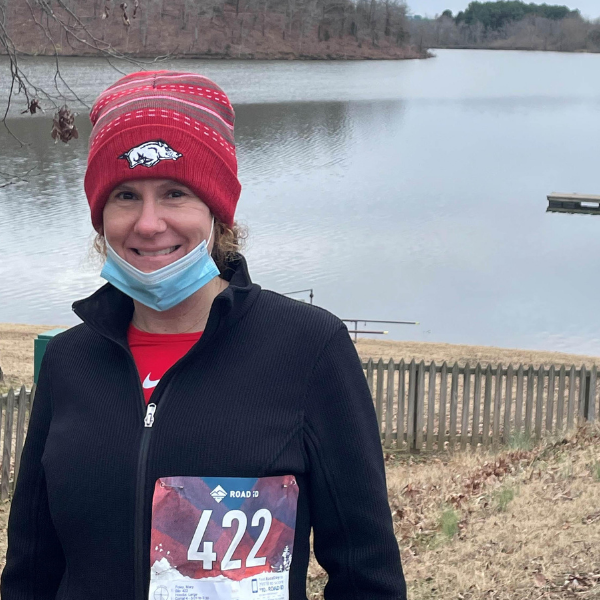 woman with marathon tag and mask in front of lake