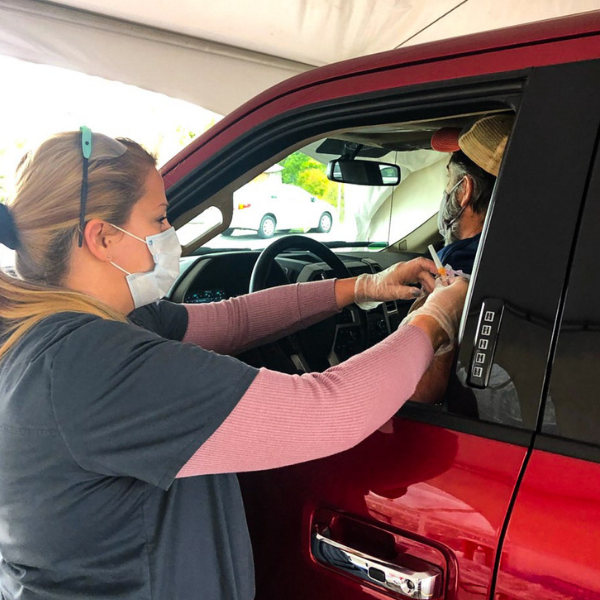 VNA nurse in mask administering vaccine to man in car